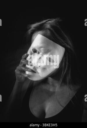 Portrait noir et blanc longue exposition d'une femme tenant un masque translucide avec flou de mouvement Banque D'Images