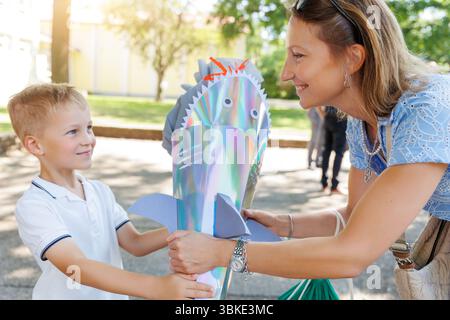 Maman heureuse donnant le fils souriant garçon tient Schultuete coloré en forme de requin rempli de cadeaux son premier jour d'école Allemagne. Cône brillant avec ailettes Banque D'Images
