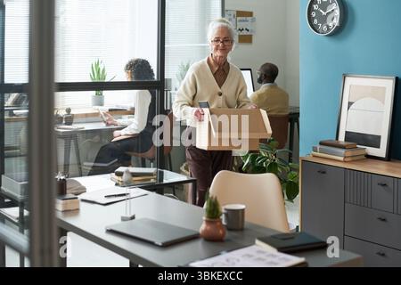 Femme caucasienne senior portant la boîte en carton tout en quittant le bureau moderne Banque D'Images