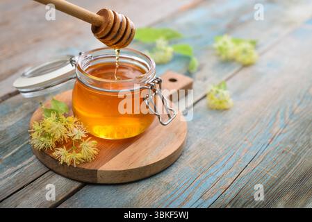 Miel de linden dans un pot en verre avec un plongeur de miel en bois et fleur de tilleul sur fond en bois Banque D'Images
