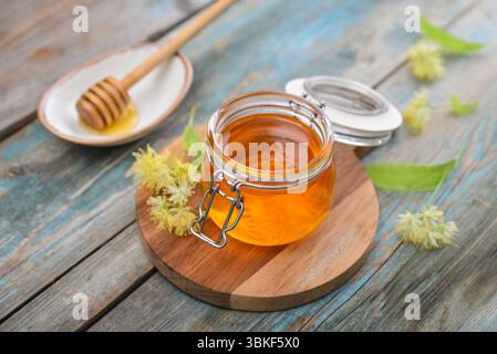 Miel de linden dans un pot en verre avec un plongeur de miel en bois et fleur de tilleul sur fond en bois Banque D'Images