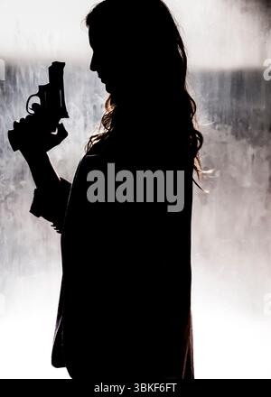 Une femme silhouette tient une arme de poing, se préparant peut-être à se défendre ou à agir dans une situation dangereuse. Banque D'Images
