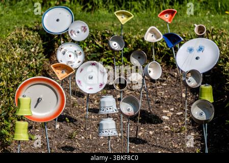 Plaques sur poteaux dans un jardin avant en France, Nouvelle-Aquitaine. Le motif correspond au proverbe allemand 'Über den Tellerrand schauen' (regardez au-delà du bord de votre assiette), qui fait référence à une attitude ouverte et curieuse dans laquelle on est prêt à transcender ses propres frontières et à apprendre de nouvelles choses. La phrase est souvent utilisée en relation avec le cosmopolitisme, un changement de perspective ou une innovation. Penser hors de la boîte. L'installation décorative de jardin comprend différentes pièces de vaisselle attachées à des bâtons et placées dans un parterre de fleurs pour créer une scène ludique et artistique. L'installation est Banque D'Images