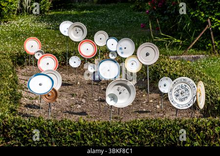 Plaques sur poteaux dans un jardin avant en France, Nouvelle-Aquitaine. Le motif correspond au proverbe allemand 'Über den Tellerrand schauen' (regardez au-delà du bord de votre assiette), qui fait référence à une attitude ouverte et curieuse dans laquelle on est prêt à transcender ses propres frontières et à apprendre de nouvelles choses. La phrase est souvent utilisée en relation avec le cosmopolitisme, un changement de perspective ou une innovation. Penser hors de la boîte. L'installation décorative de jardin comprend différentes pièces de vaisselle attachées à des bâtons et placées dans un parterre de fleurs pour créer une scène ludique et artistique. L'installation est Banque D'Images
