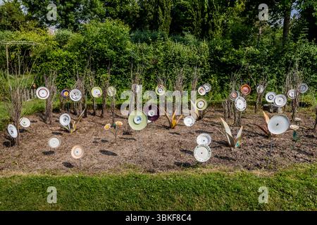 Plaques sur poteaux dans un jardin avant en France, Nouvelle-Aquitaine. Le motif correspond au proverbe allemand 'Über den Tellerrand schauen' (regardez au-delà du bord de votre assiette), qui fait référence à une attitude ouverte et curieuse dans laquelle on est prêt à transcender ses propres frontières et à apprendre de nouvelles choses. La phrase est souvent utilisée en relation avec le cosmopolitisme, un changement de perspective ou une innovation. Penser hors de la boîte. L'installation décorative de jardin comprend différentes pièces de vaisselle attachées à des bâtons et placées dans un parterre de fleurs pour créer une scène ludique et artistique. L'installation est Banque D'Images