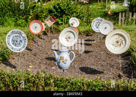 Plaques sur poteaux dans un jardin avant en France, Nouvelle-Aquitaine. Le motif correspond au proverbe allemand 'Über den Tellerrand schauen' (regardez au-delà du bord de votre assiette), qui fait référence à une attitude ouverte et curieuse dans laquelle on est prêt à transcender ses propres frontières et à apprendre de nouvelles choses. La phrase est souvent utilisée en relation avec le cosmopolitisme, un changement de perspective ou une innovation. Penser hors de la boîte. L'installation décorative de jardin comprend différentes pièces de vaisselle attachées à des bâtons et placées dans un parterre de fleurs pour créer une scène ludique et artistique. L'installation est Banque D'Images
