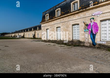 La façade de la Corderie Royale rue Toufaire à Rochefort : l'ancien atelier de corderie de l'Arsenal Royal Naval (XVIIe siècle) de 374 mètres de long s'étend au loin en arrière-plan. Sur le côté droit de l'image se trouve une installation Street art représentant l'écrivain et officier de marine Pierre Loti (1850-1923) né à Rochefort. Rue Toufaire, Rochefort, Charente-maritime, Nouvelle-Aquitaine, France Banque D'Images