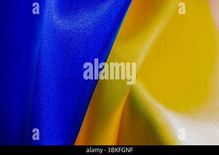 Un gros plan met en valeur un tissu satiné bleu et jaune dans une composition abstraite, des textures douces et des plis doux, rappelant un drapeau ukrainien. Banque D'Images