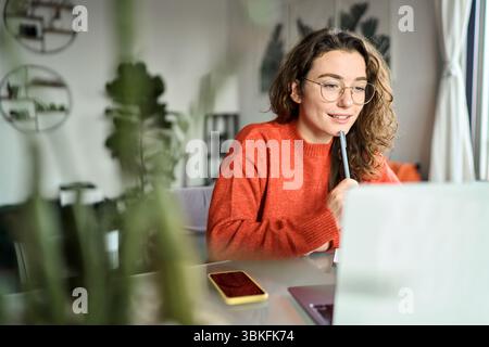 Jeune femme souriante étudiant utilisant un ordinateur portable regardant des webinars écrire à la maison. Banque D'Images