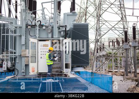 Un ingénieur effectue une inspection sur un grand transformateur à la sous-station électrique assurant la sécurité et la fonctionnalité dans un environnement industriel avec complexe Banque D'Images
