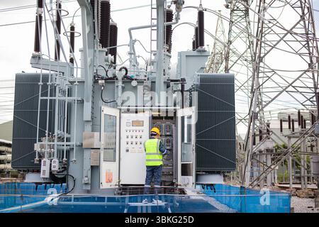 Un ingénieur effectue une inspection sur un grand transformateur à la sous-station électrique assurant la sécurité et la fonctionnalité dans un environnement industriel avec la puissance L. Banque D'Images