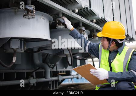 Un ingénieur effectue une inspection sur le système de refroidissement du transformateur à la sous-station électrique en assurant la sécurité et l'efficacité avec une attention et une prote minutieuses Banque D'Images