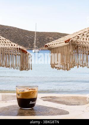 Grec Freddo Espresso sous un parapluie tissé sur la plage de Vathi, île de Sifnos Banque D'Images