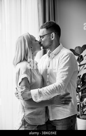 Charmant couple embrassant et serrant à la maison. Vue rapprochée des jeunes mariés avec les yeux fermés. Belle femme et homme en vêtements décontractés. Image en noir et blanc. Banque D'Images