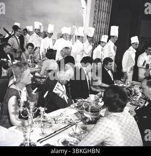 Années 1960, historique, banquet d'hôtel, dans une salle à manger, les chefs marchent devant les invités assis les uns en face des autres à de longues tables, Angleterre, Royaume-Uni. Banque D'Images