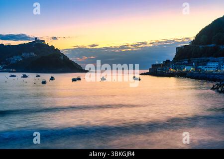 Beau coucher de soleil sur la côte de la ville de Saint-Sébastien avec de petits bateaux ancrés dans l'eau, Guipuzcoa. Banque D'Images