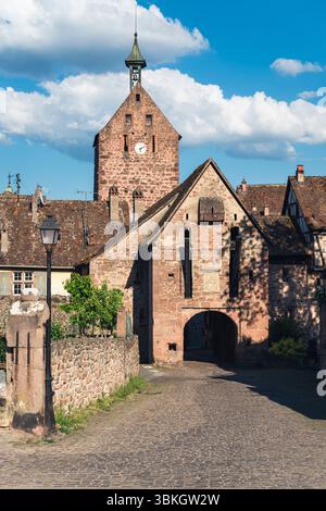 La porte médiévale de la ville haute et la tour de guet Dolder dans le centre de la vieille ville de Riquewihr brillent rouge dans le soleil de l'après-midi, Alsace, France Banque D'Images