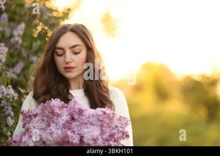 Belle femme avec des fleurs de lilas à l'extérieur le matin. Espace pour le texte Banque D'Images