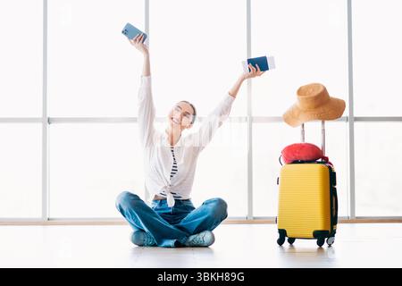 Jeune femme excitée posant avec des essentiels de voyage dans un terminal d'aéroport prêt pour un nouveau voyage ou des vacances Banque D'Images