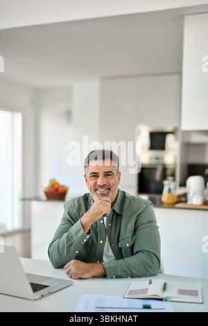 Heureux homme âgé d'âge moyen assis avec un ordinateur portable à la table de la maison. Portrait. Banque D'Images