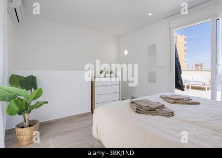Chambre lumineuse à l'étage avec décoration claire, accès balcon, grande plante et lumière naturelle. Banque D'Images