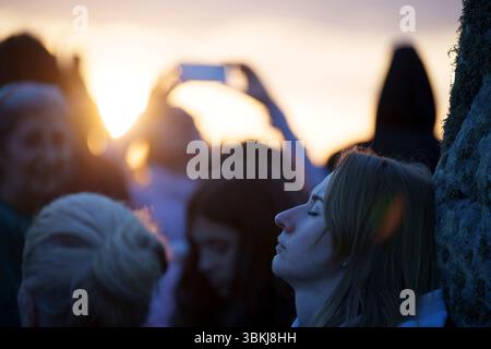 Les fêtards spirituels regardent le soleil levant et célèbrent le solstice d'été (mi-été et jour le plus long) parmi les anciennes pierres du néolithique tardif de Stonehenge, le 21 juin 2025, dans le Wiltshire, en Angleterre. Le solstice d'été est le jour le plus long de l'hémisphère nord et la nuit la plus courte de l'année, lorsque l'axe de la terre est incliné à son point le plus proche du soleil et les païens disent que l'ancien monument est un lieu sacré qui relie la Terre, la Lune, le Soleil et les saisons. Stonehenge a été construit en trois phases entre 3 000 av. J.-C. et 1 600 av. J.-C. et est maintenant la propriété de English Heritage qui dit que 25 000 visiteurs étaient Banque D'Images