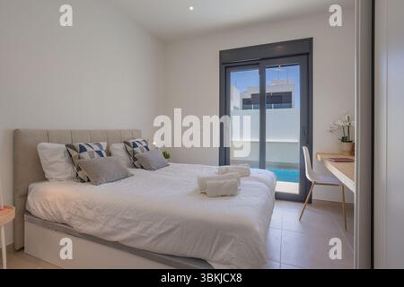 Chambre moderne avec lit double, vue sur la piscine par des portes coulissantes et bureau en bois intégré. Banque D'Images