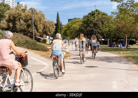 Les gens de différents âges font du vélo le long d'un large chemin de parc par une journée ensoleillée, mode de vie actif, vélos de ville - Valence, Espagne, 05.06.2023 Banque D'Images