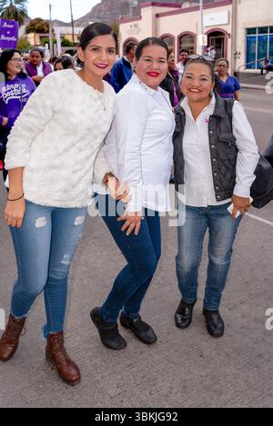 Trois femmes au maquillage lourd portant des jeans bleus et des chemises blanches posent dans les rues de Guaymas, Sonora, Mexique. Banque D'Images