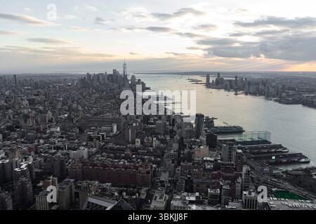 L'image capture une vue aérienne de New York au coucher du soleil, mettant en valeur son horizon dense et le front de mer. Le soleil couchant projette une lueur chaude sur th Banque D'Images