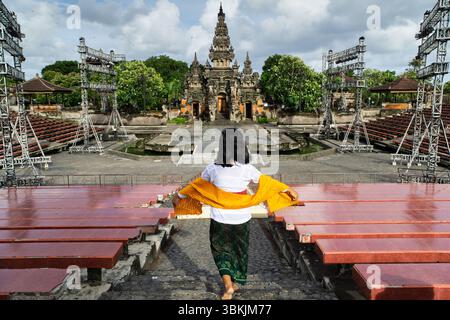 Une femme en tenue traditionnelle balinaise approche du bâtiment orné de Ksirarnawa au Bali’s Art Center à Denpasar, encadré par un échafaudage événementiel Banque D'Images