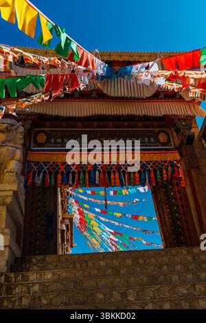 Architecture du monastère de Songzanlin avec des drapeaux de prière colorés flottant contre un ciel bleu clair. Banque D'Images