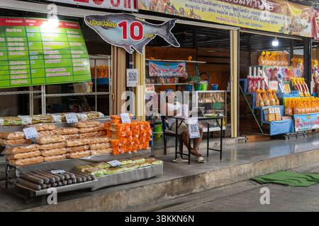 Vue générale d'un magasin vendant de la nourriture pour nourrir les poissons et divers articles à offrir au temple, avec un vendeur assis sur une chaise, au marché flottant de Khwan Riam. Khwan Riam Floating Market est un marché de style moderne avec des attractions au bord du canal, des stands fixes et des bateaux-restaurants ancrés, sans le commerce traditionnel de bateau à bateau. Son nom vient de Phlae Kao, un roman d'amour thaïlandais classique et un film de 1977, racontant l'histoire d'amour tragique de Khwan et Riam, amoureux séparés par l'opposition familiale. Le marché est divisé en deux parties par les temples Wat Bang Peng Nuea et Wat Bang Peng Tai, connecte Banque D'Images