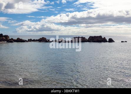 Les eaux calmes se tapissent doucement contre une ligne de rochers altérés, créant une scène côtière tranquille sous le ciel nuageux Banque D'Images