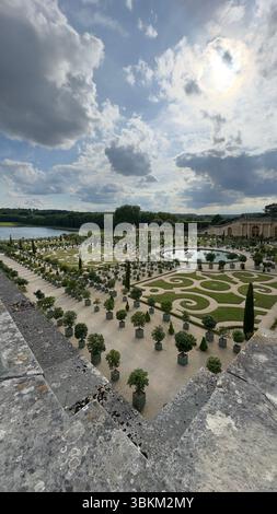 Vue surélevée d'un jardin formel avec des motifs géométriques, un étang circulaire, et des arbres bien entretenus sous un ciel nuageux. Banque D'Images