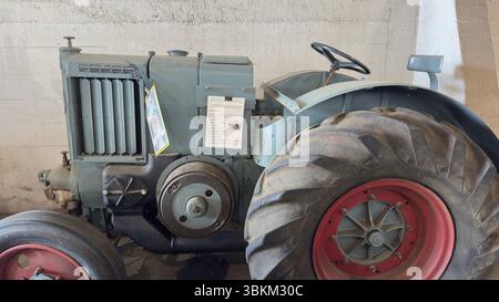 Un tracteur gris vintage est partiellement visible, avec un accent sur le pneu avant et le grand pneu arrière. Un panneau est fixé à la carrosserie du tracteur. Banque D'Images