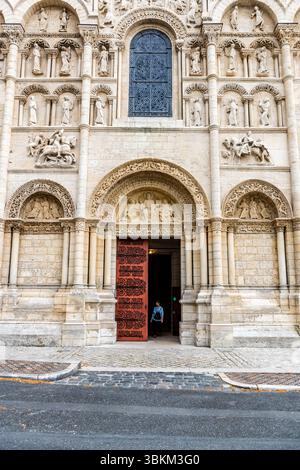 Façade ouest de la cathédrale Saint-Pierre d’Angoulême (XIIe siècle) : les archivoltes à plusieurs niveaux et les niches figuratives du portail principal présentent un décor figuratif roman ; les portes en bois rouge de l’entrée principale sont ouvertes et une personne quitte le bâtiment. La cathédrale est classée « Monument historique » et fait partie de la voie de St James (via Turonensis). Place Saint-Pierre, Angoulême, Nouvelle-Aquitaine, France Banque D'Images
