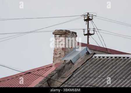 Une cheminée en brique altérée et une toiture en métal rouillé se dressent contre un ciel gris, entrecoupé par des lignes électriques, mettant en valeur un simple extérieur rural ou urbain SC Banque D'Images