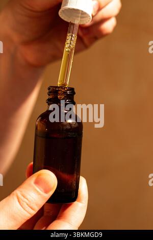 Femme main à l'aide d'une pipette pour distribuer de l'huile faciale de luxe sur fond neutre. Parfait pour les routines de soins de la peau annonces de produits cosmétiques de beauté biologiques. Banque D'Images