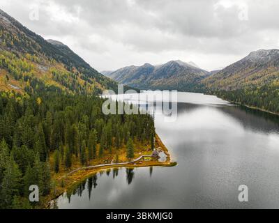Le rivage serein du lac Rakhmanovskoe, bordé par de denses forêts d'automne, comprend un petit hangar à bateaux et un sentier Banque D'Images