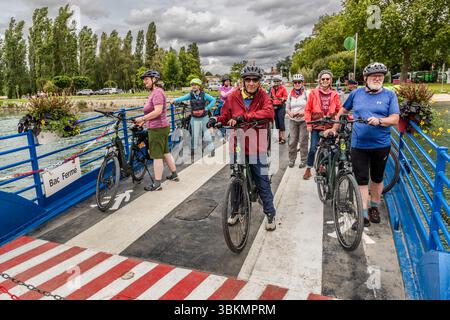 Le groupe de cyclistes de Die Landpartie se tient avec leurs vélos électriques sur le bac de Chaniers (Bac de Chaniers), qui traverse la Charente. Parmi eux se trouvent la journaliste Angela Berg (deuxième à droite, en veste rouge) et la guide touristique Katell Nicoux (à l'arrière à gauche, casque vert). Le bac fonctionne à la D138, Chaniers, Nouvelle-Aquitaine, France, et relie le village à Courcoury sur la rive opposée. La traversée remonte au Moyen Âge et est gratuite pour les piétons, cyclistes et véhicules. Un panneau sur la rambarde bleue indique "Bac fermé". En anglais : "Ferry closed". La scène montre une atmosphère détendue Banque D'Images