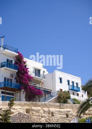 Maisons grecques traditionnelles à Adamas, île de Milos, avec façades blanchies à la chaux, balcons bleus et bougainvilliers en fleurs sous un ciel sans nuages. Banque D'Images