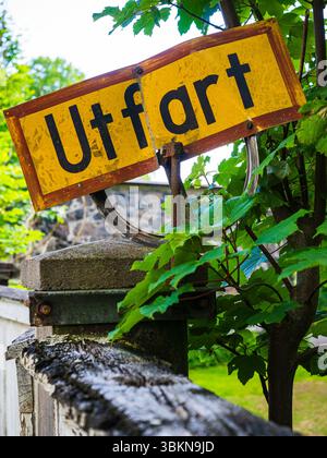 Un panneau de sortie jaune affichant le mot Utfart se distingue des feuilles vertes vives. Le panneau est monté sur un poteau, indiquant un emplacement proche Banque D'Images