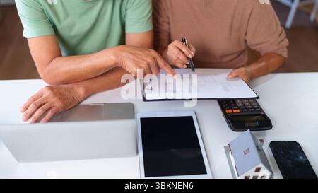 Couple plus âgé examinant les documents financiers dans leur maison. Ils planifient ensemble l'épargne-retraite et les placements immobiliers. Ils utilisent la technologie Banque D'Images