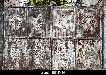 Portail en fer forgé rouillé avec motifs géométriques décoratifs et texture métallique altérée. Détail grunge, adapté aux arrière-plans. Personne. Banque D'Images