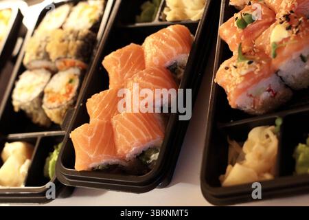 Différents types de sushis soigneusement disposés dans des boîtes à emporter noires. Gros plan sur la photo de nourriture avec garniture de saumon et condiments d'accompagnement. Idéal pour la livraison de nourriture c Banque D'Images