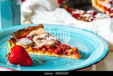 Un morceau de tarte à la rhubarbe et aux fraises sur une assiette turquoise sur la table avec une serviette blanche et une tasse de thé. Photo de haute qualité Banque D'Images