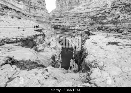 Un groupe de personnes se promène dans un canyon traversé par une rivière. Le canyon est rocheux et aride, sans végétation en vue. Le peuple Banque D'Images