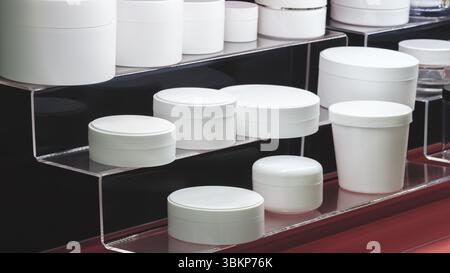Une rangée de différentes formes et tailles de bocaux en plastique vides blancs et de bouteilles de différentes formes avec des couvercles pour liquides, cosmétiques, pharmaceutiques ou domestiques Banque D'Images
