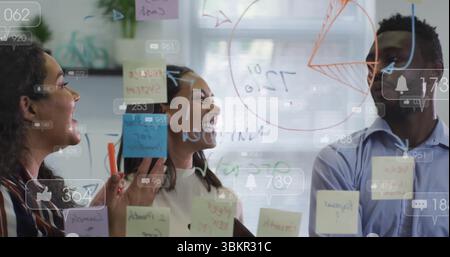 Collaboration de collègues esquissant des données sur un mur de verre au bureau, avec un graphique circulaire et des notes adhésives Banque D'Images